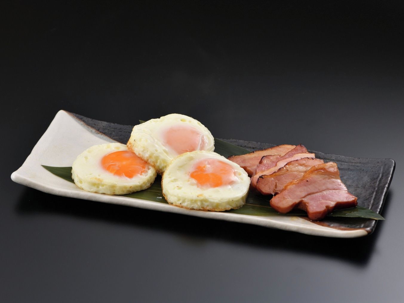 En tallerken med tre stykker tamagoyaki og en skive skinke.