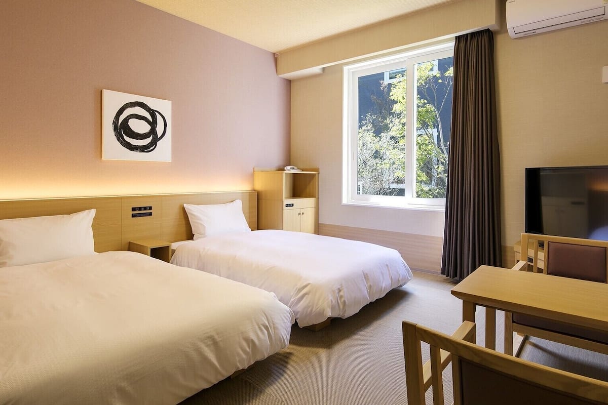 Una habitación de hotel con dos camas, un escritorio, un televisor y una ventana con cortinas.