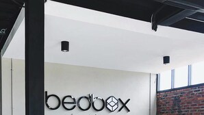 A modern interior with a bench, a wall-mounted sign reading "beabox vientiune," and a brick wall. - Bedbox Vientiane Hostel (Vientiane)