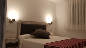 A hotel room with a bed, two wall-mounted lights, a window with blinds, and a bedside table with a lamp. - APARTMENT 1 MENCIA (MIRADORES DEL ISASA) (Herce)