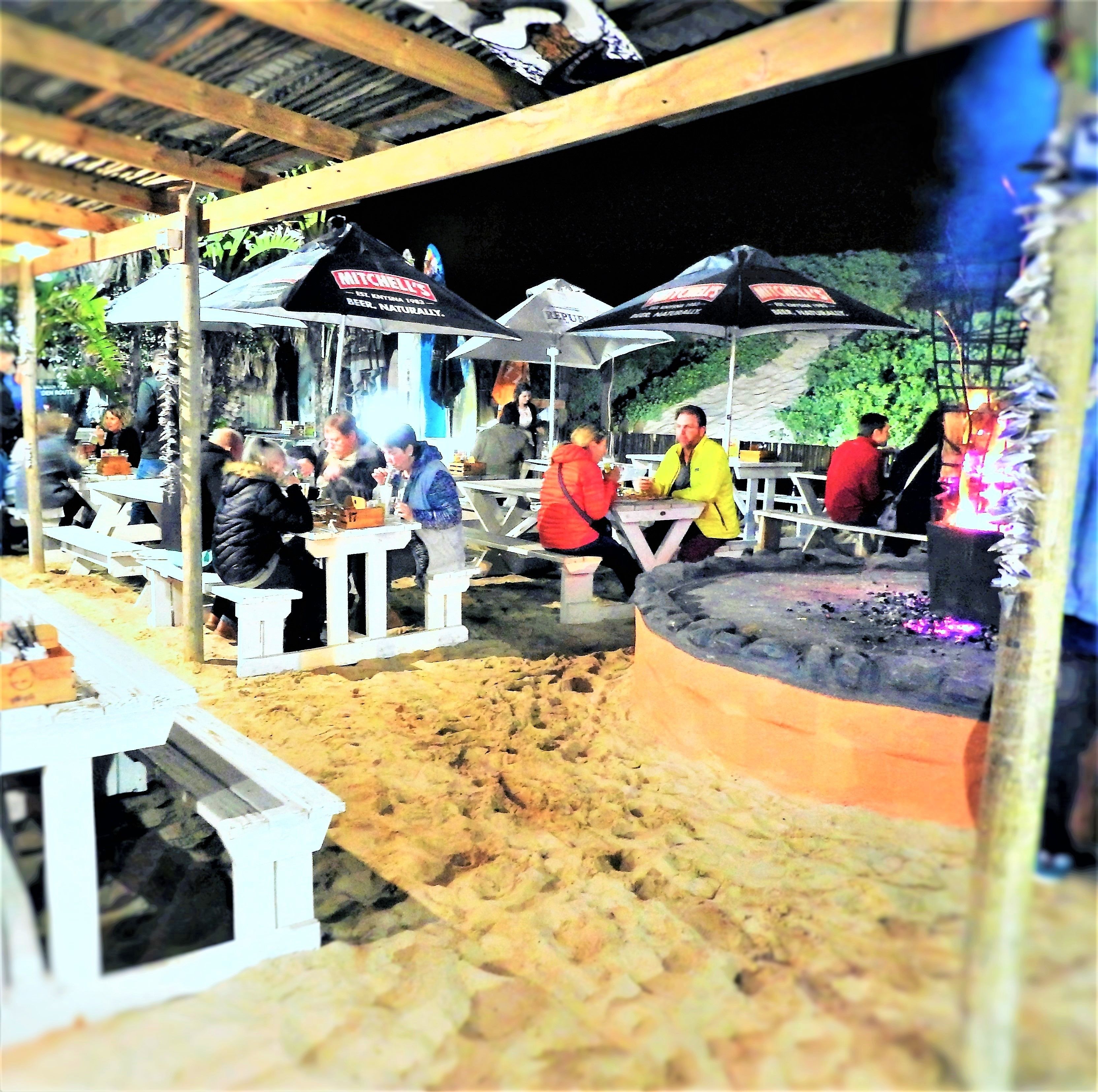 An outdoor dining area with tables and chairs, a grill, and umbrellas.
