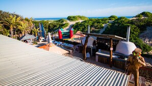 A beachside restaurant with outdoor seating, a barbecue grill, and surfboards. - Pili Pili Beach Cabanas (Sedgefield)