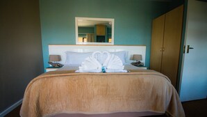 A hotel room with a large bed, a mirror above the bed, a wooden wardrobe, and two bedside lamps. - Pili Pili Beach Cabanas (Sedgefield)