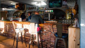 A bar area with stools, a counter, and a television mounted on the wall. - Pili Pili Beach Cabanas (Sedgefield)