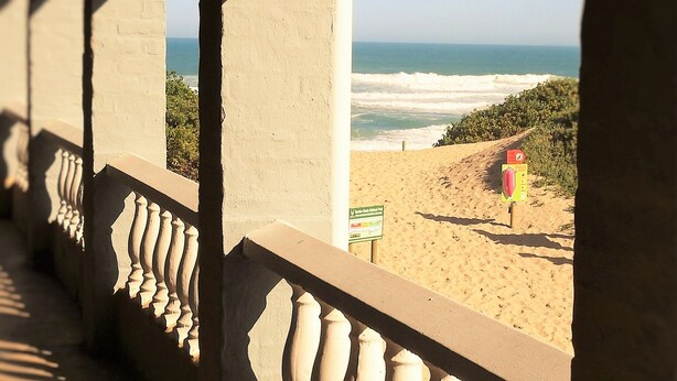 A balcony with balustrades overlooking a beach with a lifeguard tower. - Pili Pili Beach Cabanas (Sedgefield)