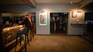 A bar area with stools, a brick wall, and a poster on the wall. - Pili Pili Beach Cabanas (Sedgefield)