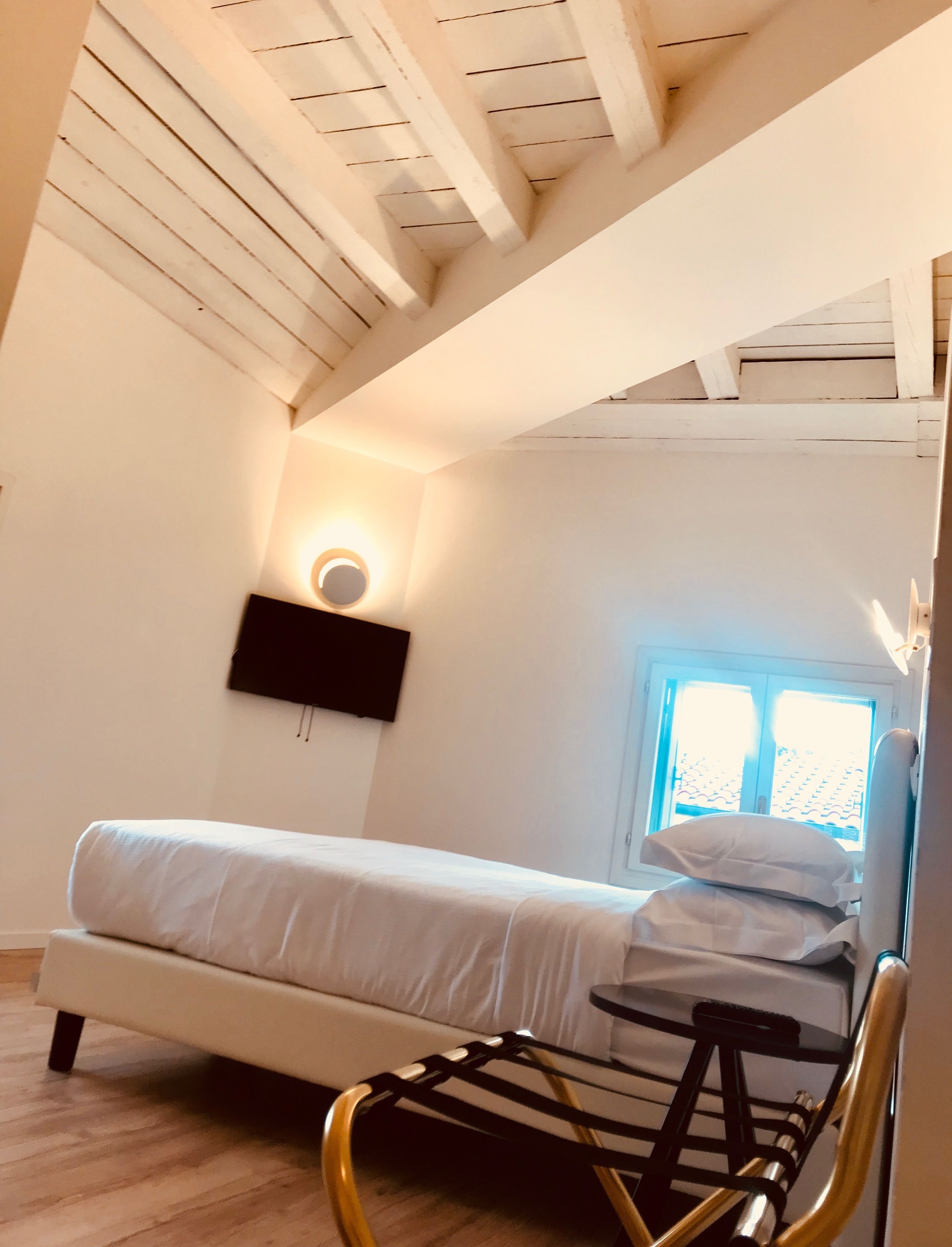 Een slaapkamer met een bed, een stoel, een tv aan de muur en een raam met zonwering.