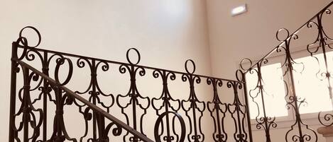 A staircase with ornate black metal railings and a beige wall.
