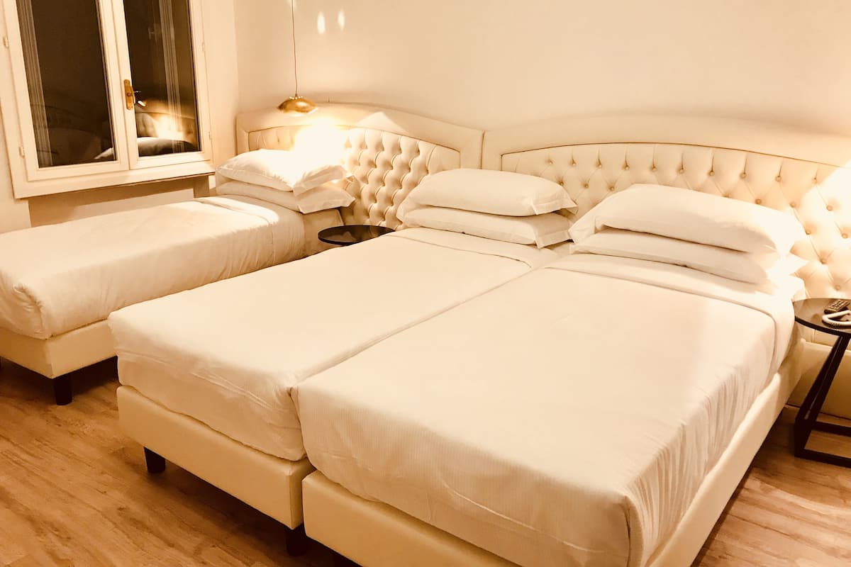Habitació d'hotel amb un llit gran, dos llits més petits, una taula de nit i una finestra.