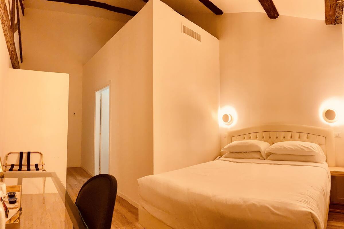 Un dormitori amb un llit, làmpades de nit, un escriptori amb una cadira i una taula petita amb una làmpada.