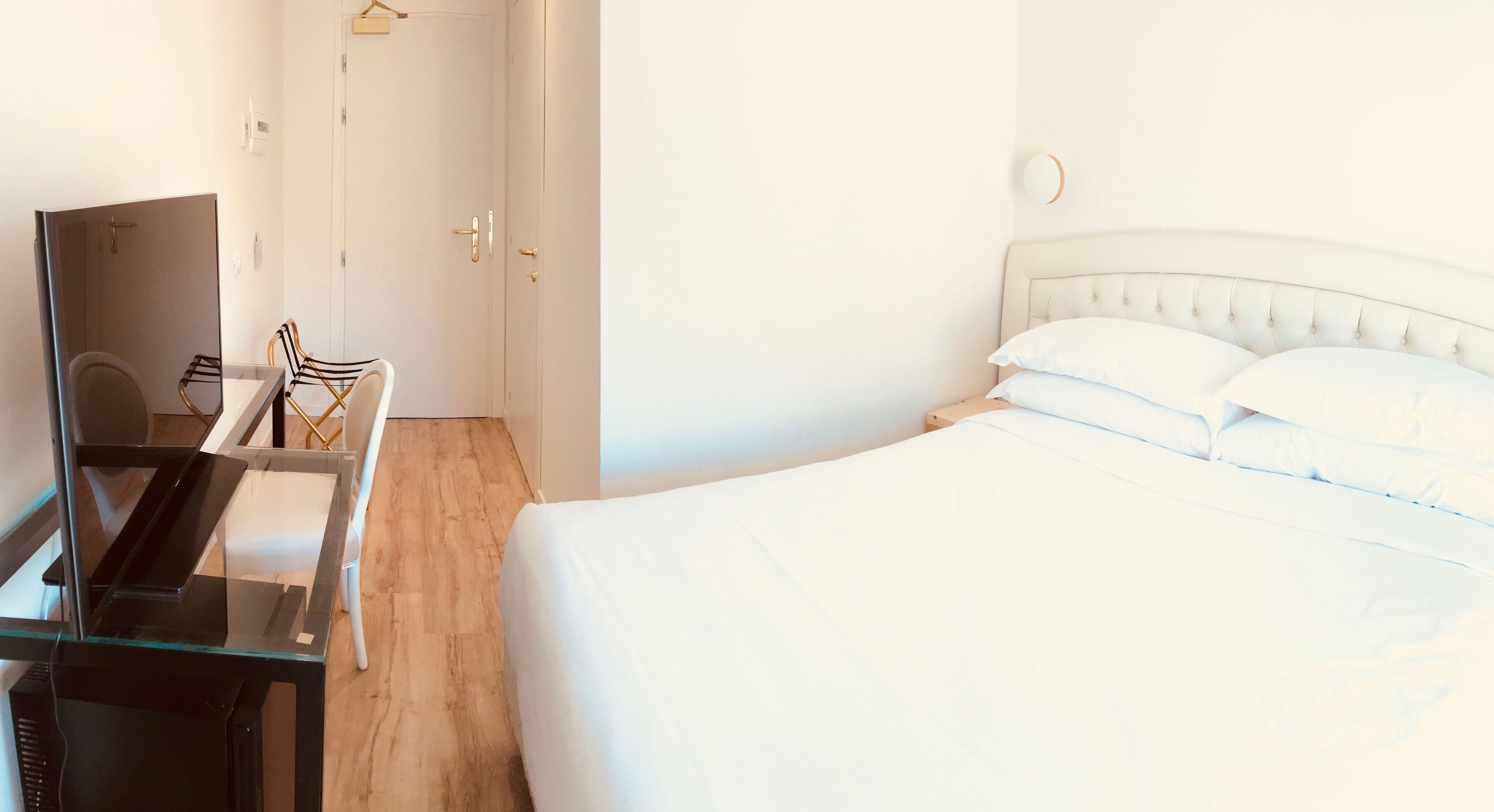 A hotel room with a bed, a desk with a chair, and a door.