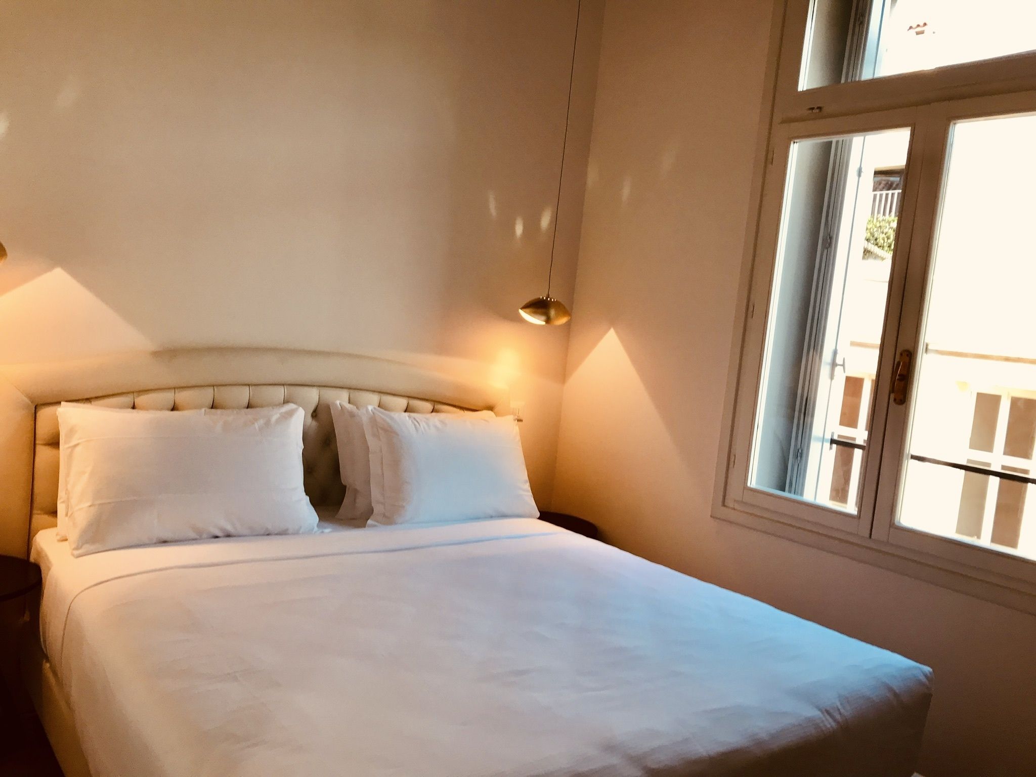 A bedroom with a bed, pillows, a nightstand, a lamp, and a window.