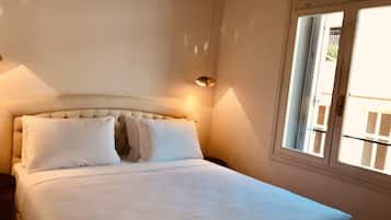 A bedroom with a bed, pillows, a nightstand, a lamp, and a window.