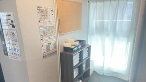 Ein Hotelzimmer mit einem Bulletinbrett, einem Ablagefach mit Handtüchern und einem Fenster mit durchsichtigen Vorhängen.