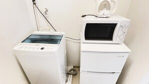 Ein kleiner Waschraum mit einer Waschmaschine mit Frontlader, einer platzsparenden Wasch-Trockner-Kombination und einem Wasserkocher auf dem Trockner.