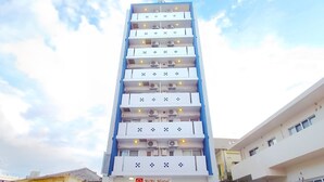 Ein hohes Hotel mit mehreren Balkonen, ein Auto davor und ein Verkaufsautomat.