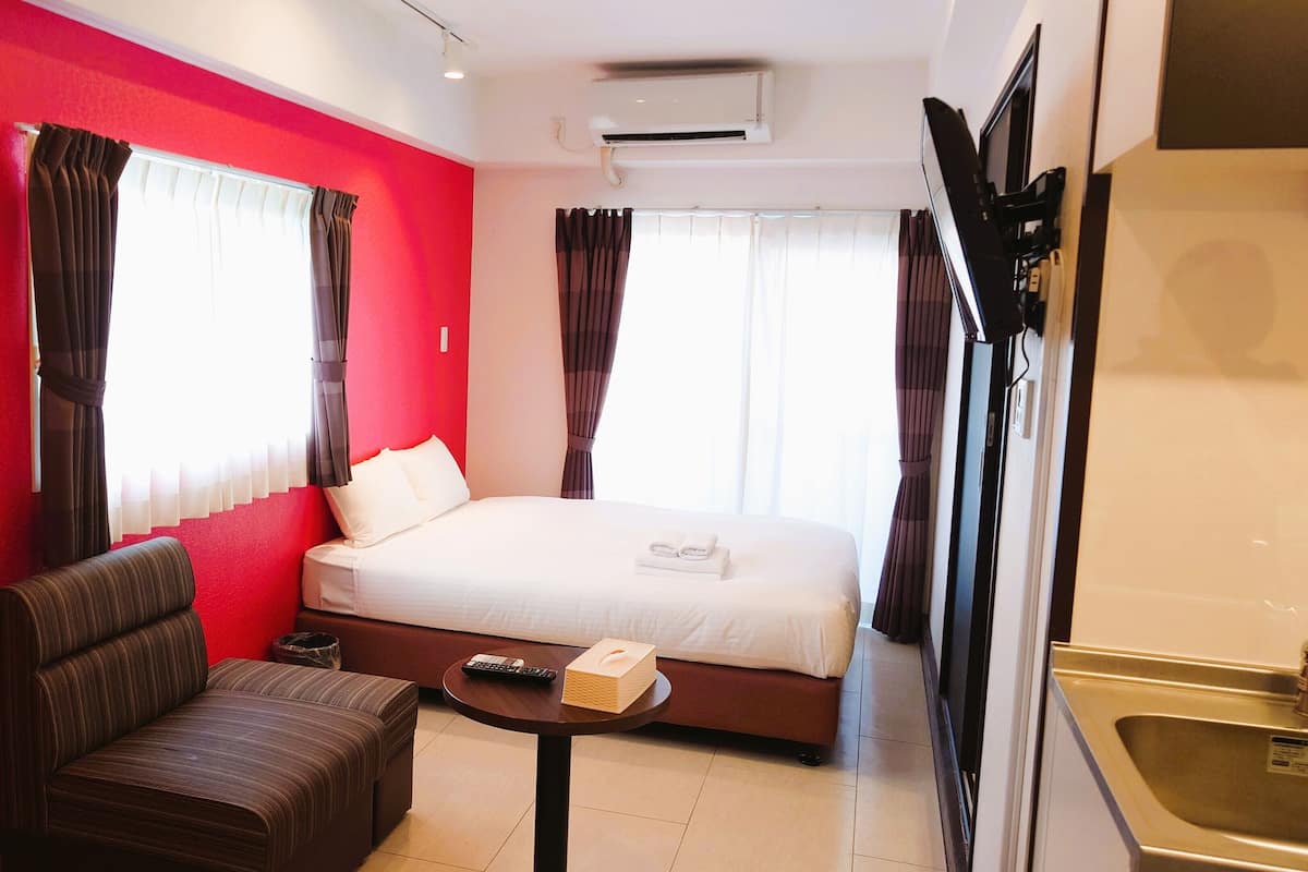 Habitació d'hotel amb una paret vermella, un llit, un sofà, una taula petita i una televisió.