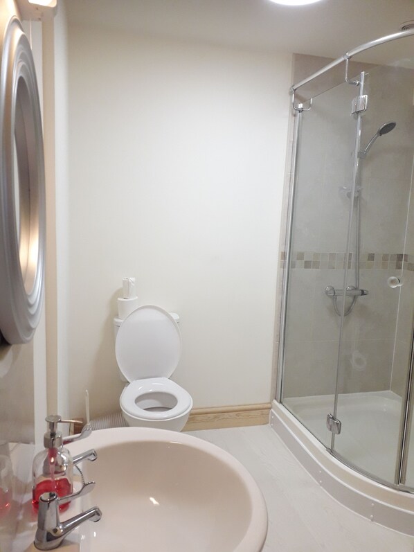 Un baño con inodoro, lavamanos y ducha con mampara de vidrio.