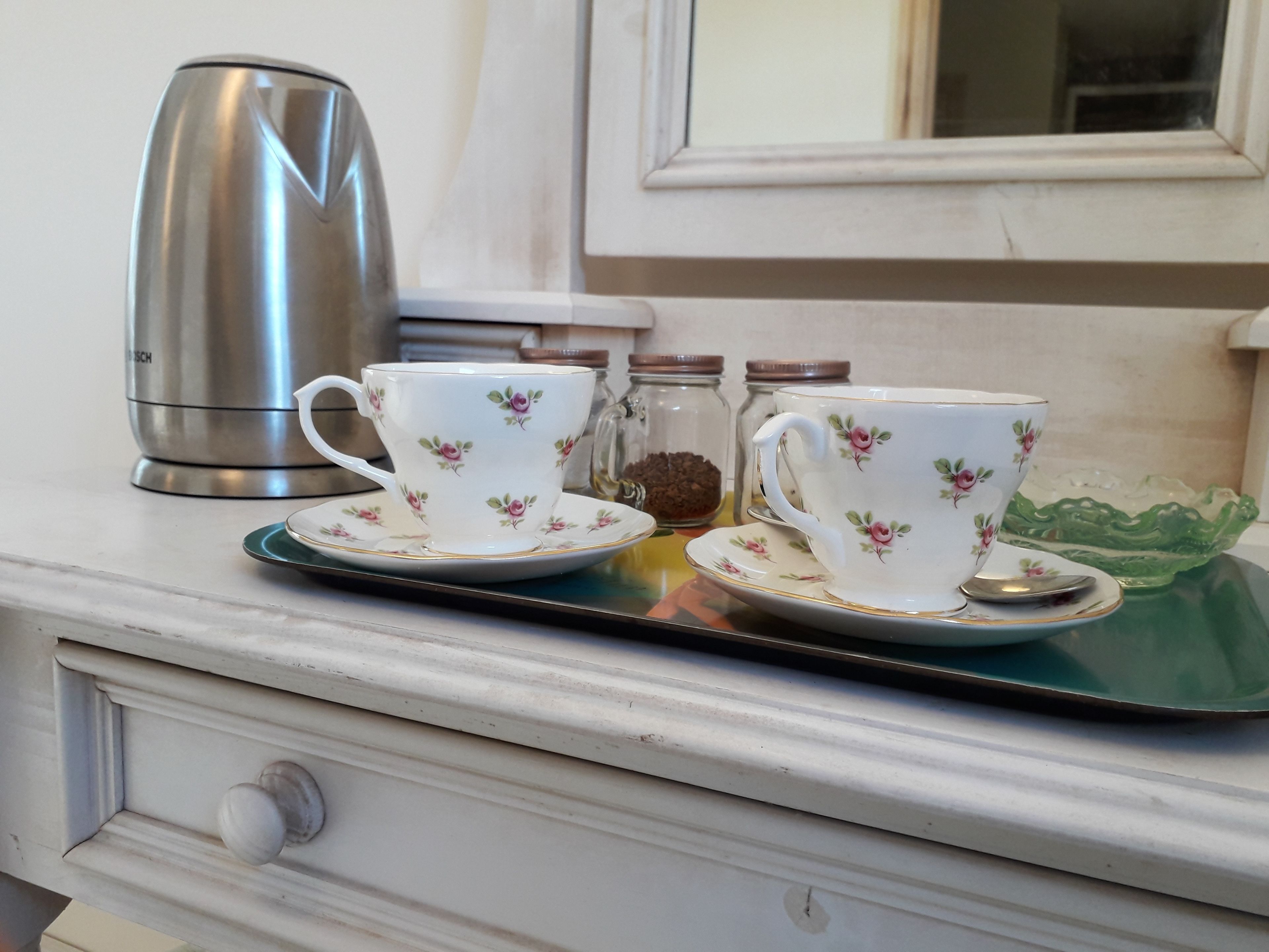 A kitchen counter with a Bosch coffee maker, two floral-patterned cups and saucers, a glass jar, and a green glass bowl.
