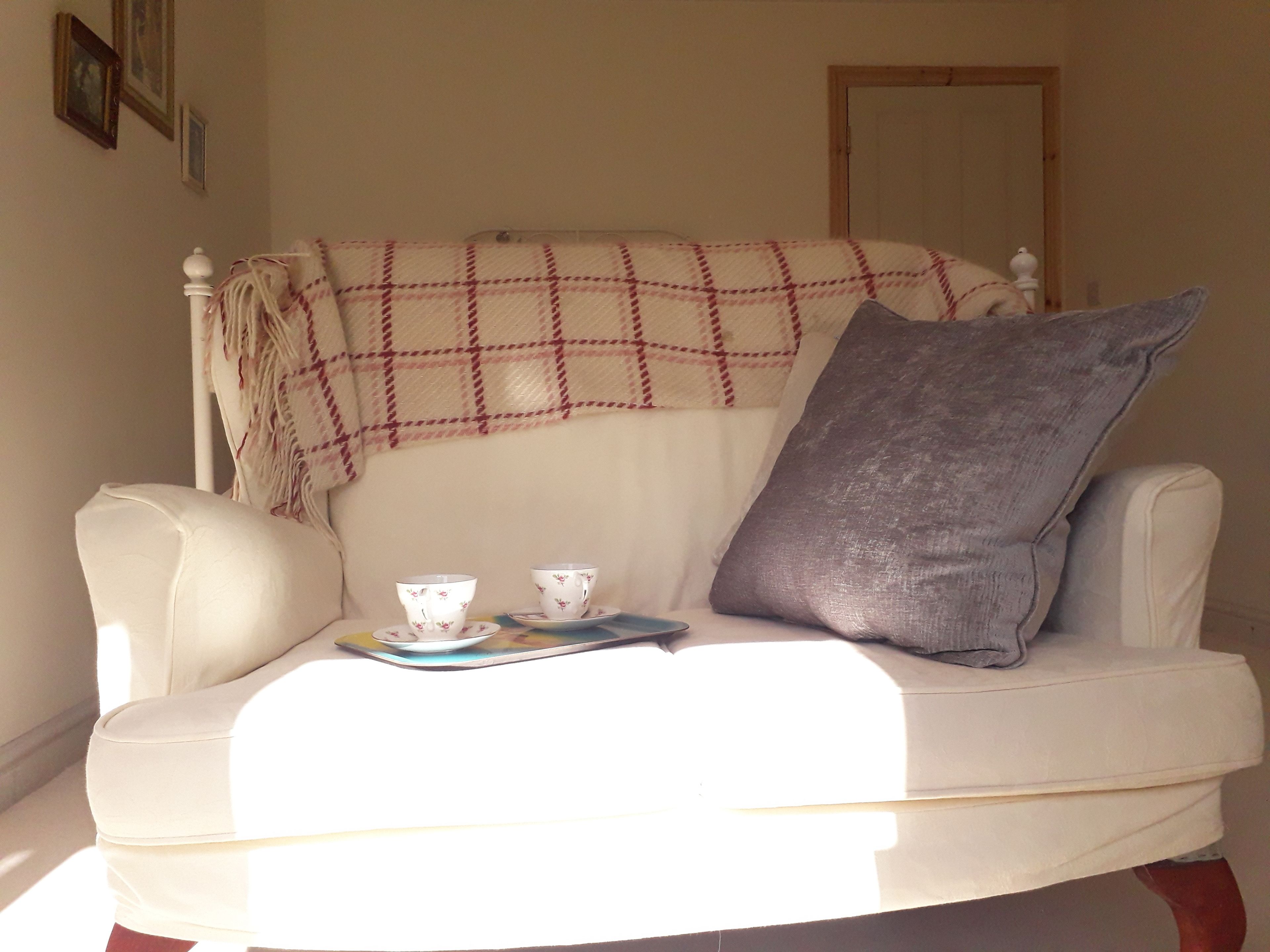 A white armchair with a plaid blanket and a pillow, a tray with two cups and a saucer, and a small book.