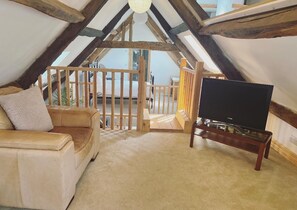 A cozy attic room with a sofa, a TV on a stand, and a wooden railing. - Melin Tregib (Llandeilo)