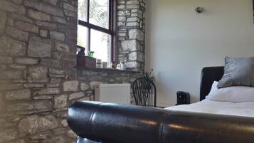 A bedroom with a stone wall, a window, a bed with pillows, a chair, and a radiator.