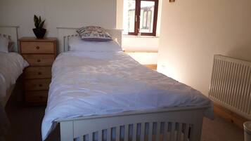 Une chambre avec un lit simple, une table de chevet ornée d’une plante, une commode et une fenêtre donnant sur l’extérieur.