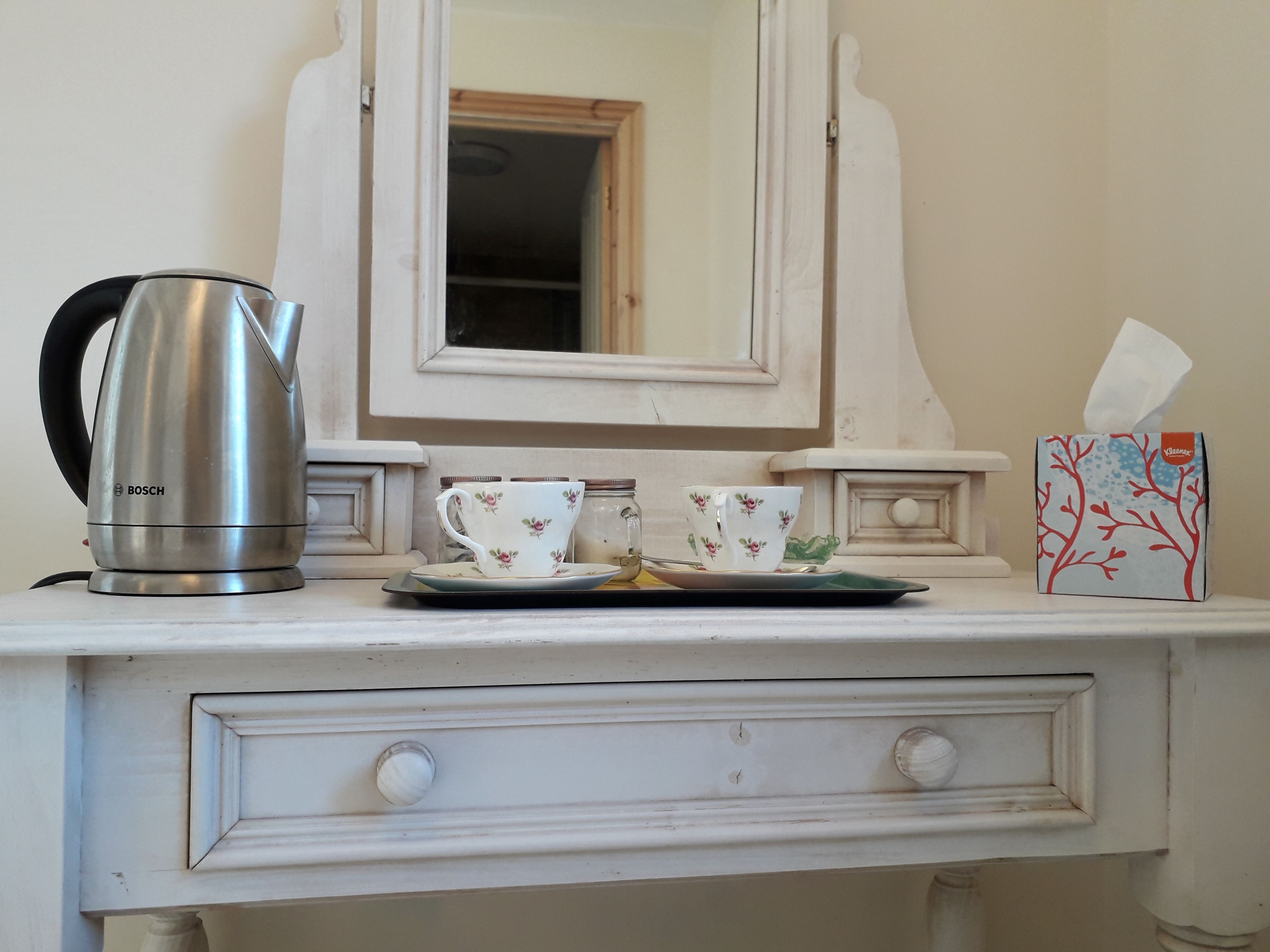 A kitchen counter with a Bosch kettle, floral tea cups, a tissue box, and a mirror above.