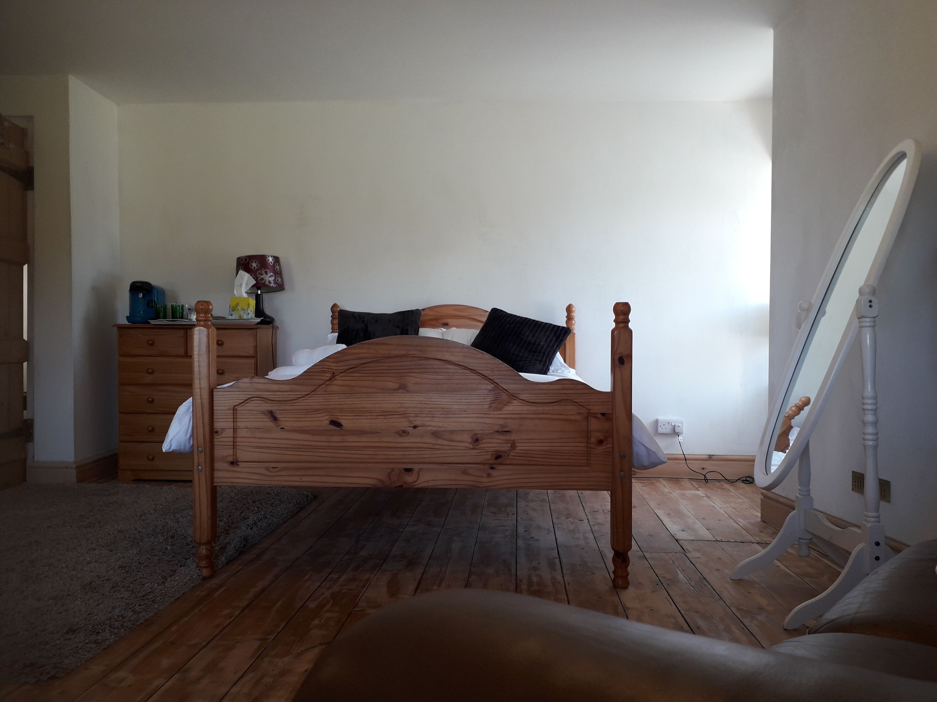A bedroom with a wooden bed, a dresser, a bedside table with a lamp, and a mirror.