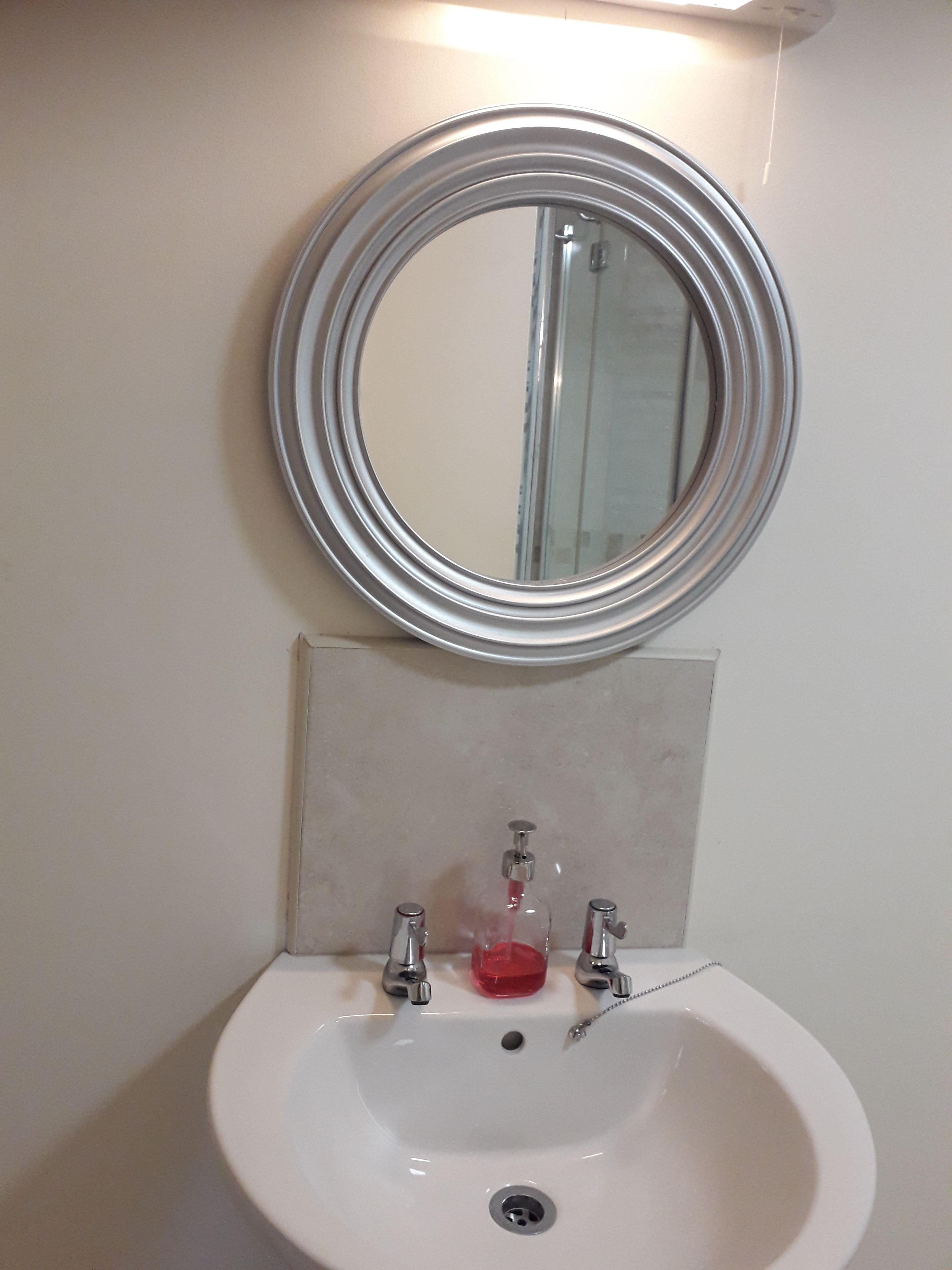 A bathroom sink with a round mirror above it, a soap dispenser, and a towel rack.