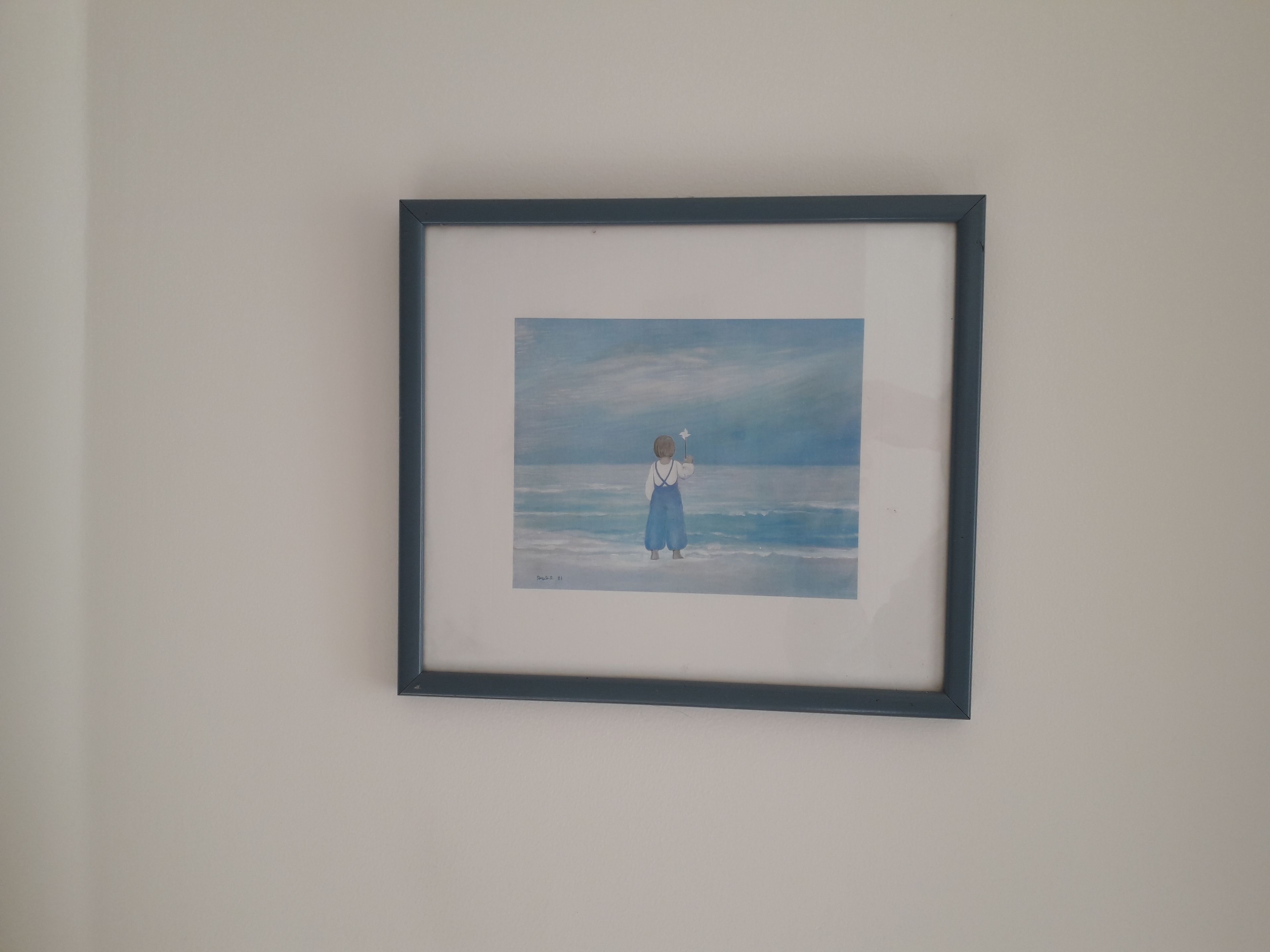 Een lijst met een kunstwerk waarop een persoon in een blauwe jurk op het strand staat, met golven op de achtergrond.