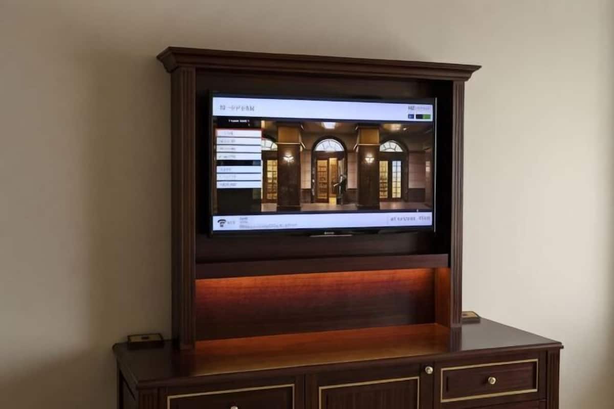 A television mounted on a wooden cabinet with a digital interface displaying a room layout.