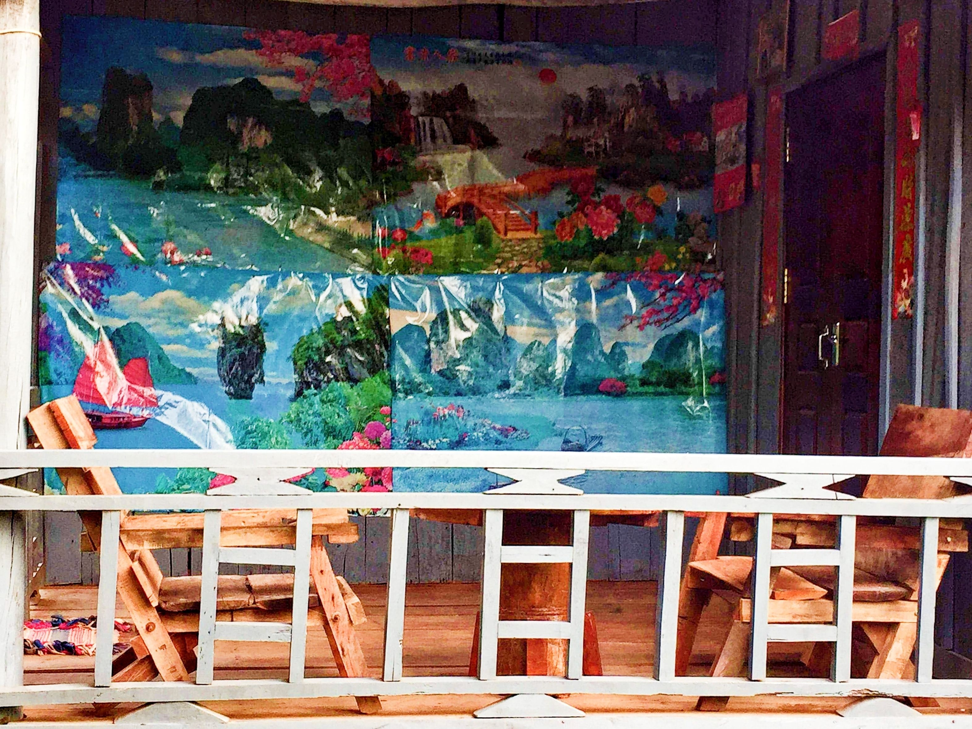 Una habitación con un cuadro grande de un paisaje, sillas de madera y una barandilla blanca.
