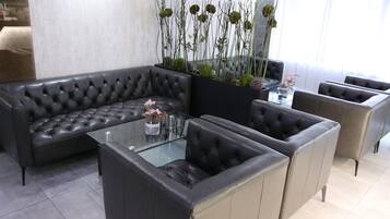 A modern living room with a black leather sectional sofa, a glass coffee table, and a decorative plant arrangement.