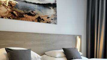 Cama bem arrumada com lençóis brancos e duas almofadas, cabeceira de madeira e uma pintura de uma praia acima da cama.