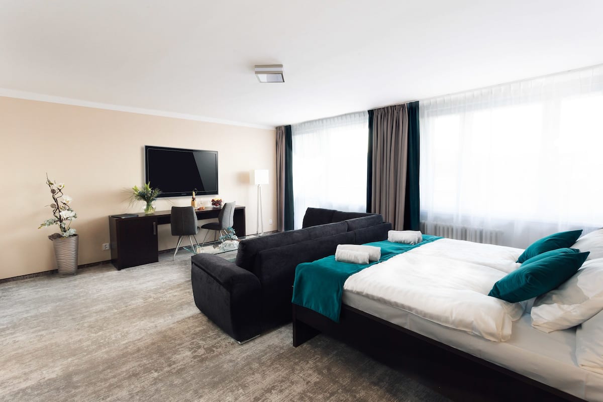 A modern hotel room with a bed, a desk, a chair, a TV, and a potted plant.