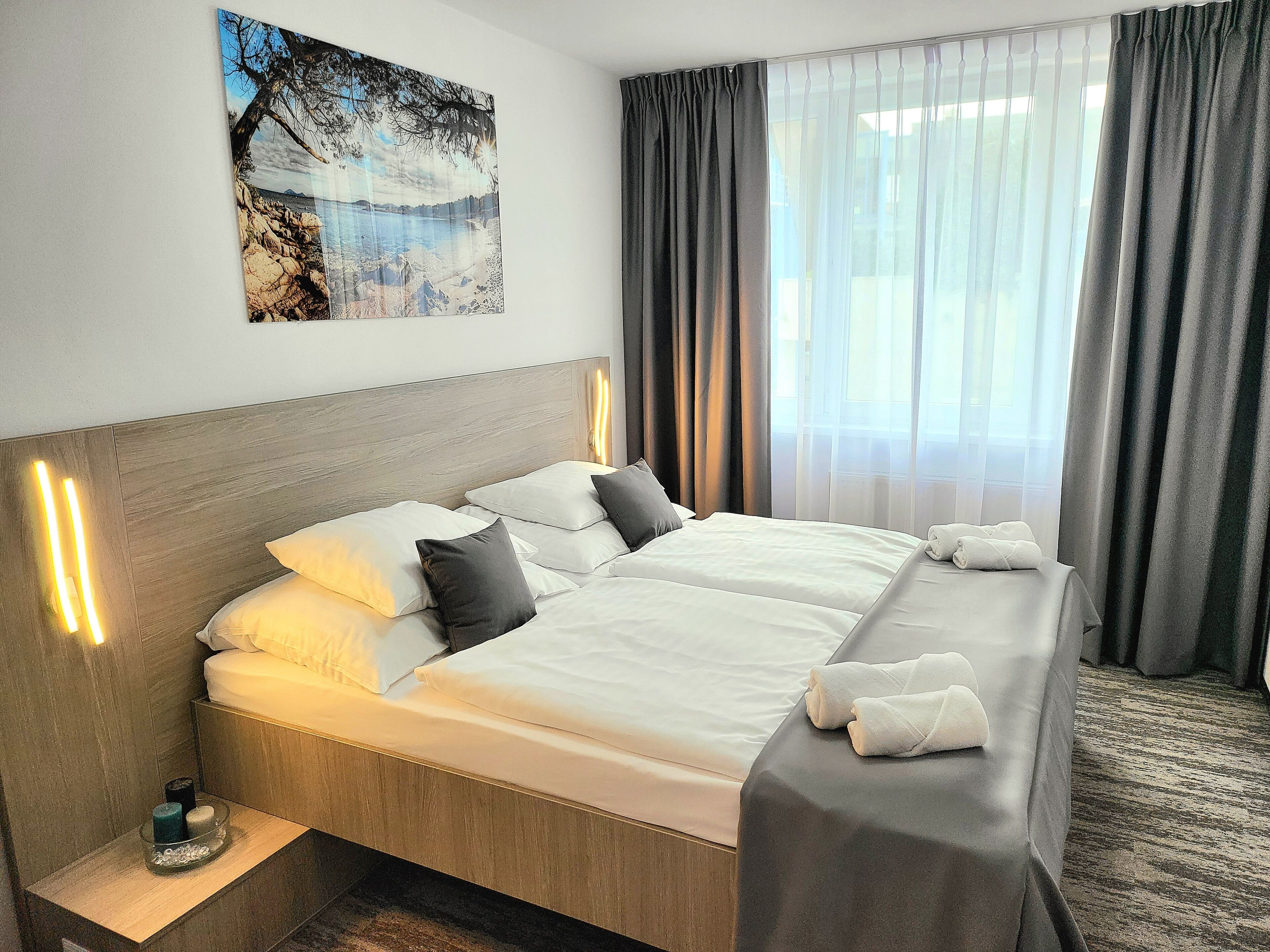 Habitación de hotel con cama doble, una mesita de noche con una vela y un cuadro en la pared.