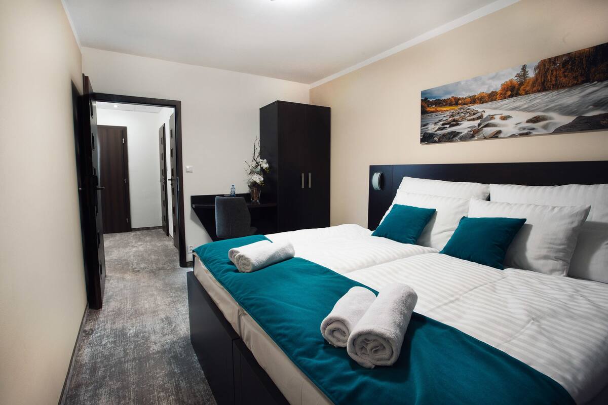 A hotel room with a large bed, a dark wardrobe, a desk with a chair, and a painting on the wall.