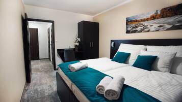 A hotel room with a large bed, a dark wardrobe, a desk with a chair, and a painting on the wall.