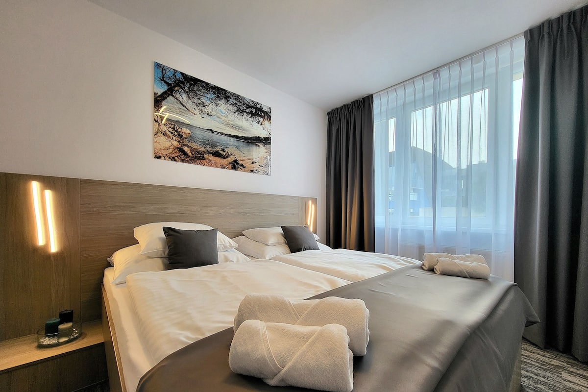 A hotel room with a large bed, a headboard, a painting on the wall, and a window with curtains.