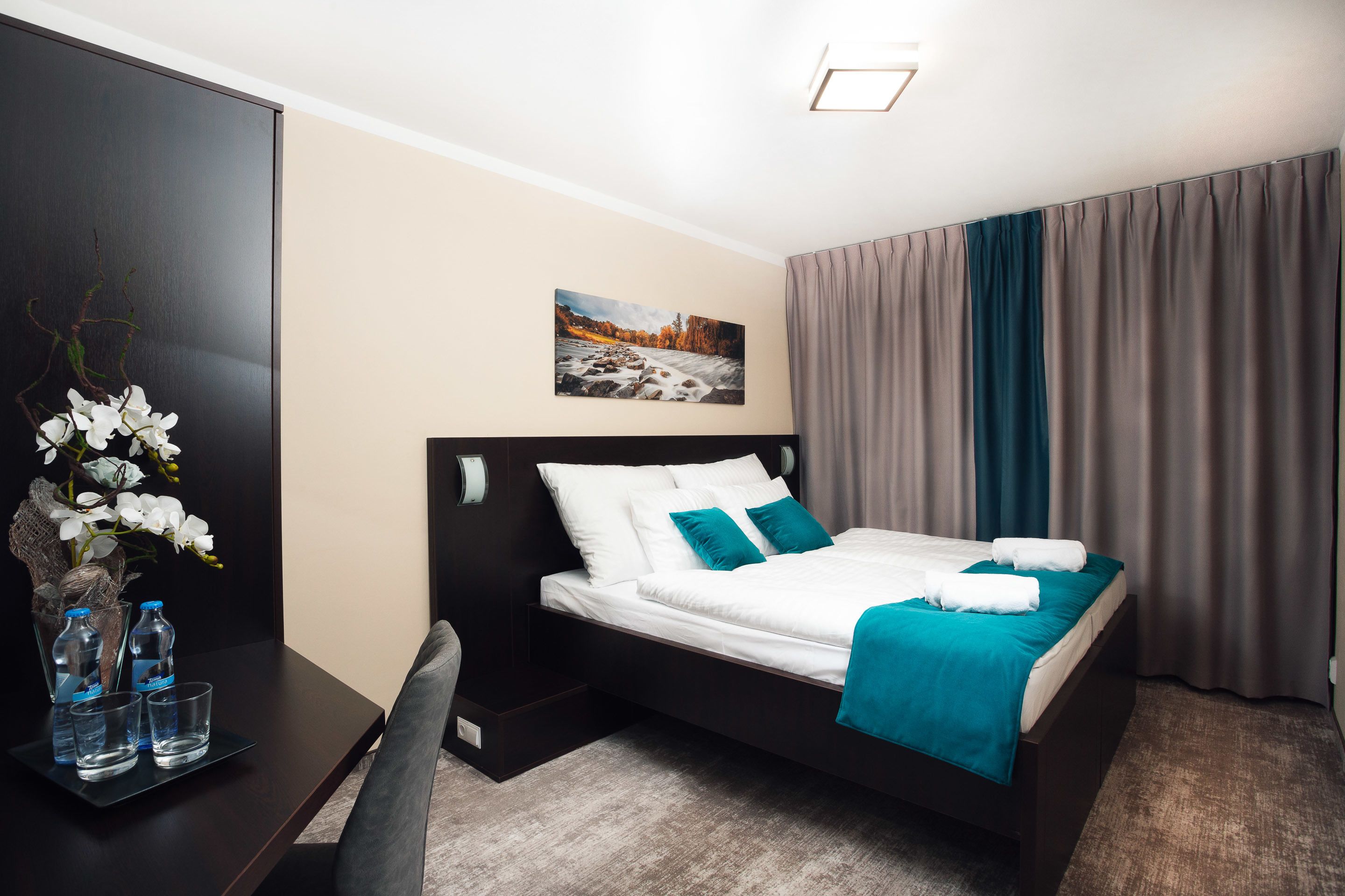A neatly arranged hotel room with a bed, a desk, and a vase of white flowers.