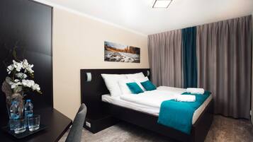 A neatly arranged hotel room with a bed, a desk, and a vase of white flowers.