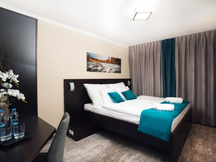 A neatly arranged hotel room with a bed, a desk, and a vase of white flowers.