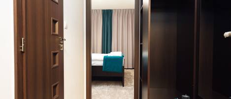 Un pasillo de hotel con un armario de madera, una cama con manta azul y una mesita con velas.