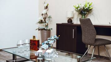 Une table en verre sur laquelle se trouvent une bouteille, deux verres et un arrangement floral décoratif. Une chaise est placée sur la droite.