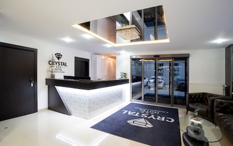 A modern hotel reception area with a reception desk, a digital screen, and a glass door entrance.
