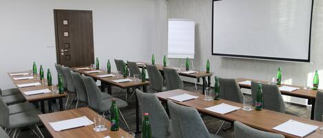 Un salón de conferencias con varias mesas, sillas y una pantalla para proyector.