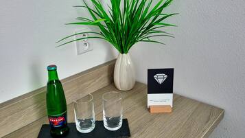 A wooden table with a green bottle, two glasses, a potted plant, and a small card.