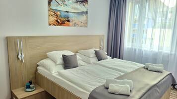 A hotel room with a large bed, a wooden headboard, a bedside table with a glass container, and a painting of a beach scene.