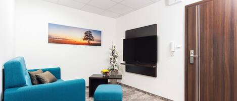 Una sala de estar moderna con un sofá color turquesa, un pequeño reposapiés, un televisor de pantalla plana montado en la pared y una puerta de madera.